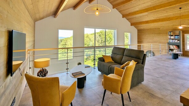 Un vaste espace de vie doté d’un plafond haut, de poutres en bois, d’un canapé, de fauteuils, d’une table basse et d’une bibliothèque.