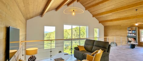 A spacious living area with a high ceiling, wooden beams, a sofa, chairs, a coffee table, and a bookshelf.