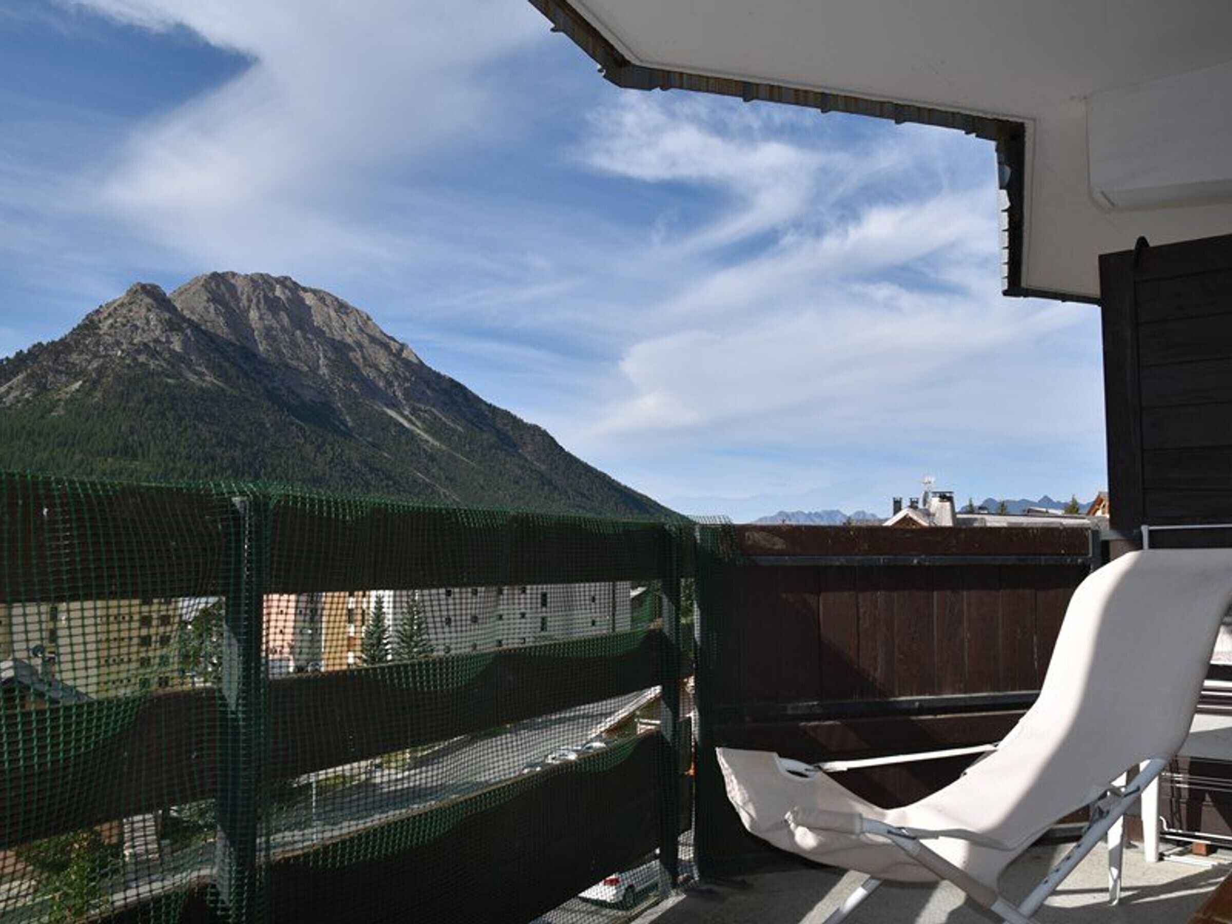 Un balcon avec une chaise blanche, un filet de sécurité vert et une vue sur la montagne.