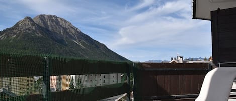 Un balcón con una silla blanca, una red de seguridad verde y vistas a la montaña.