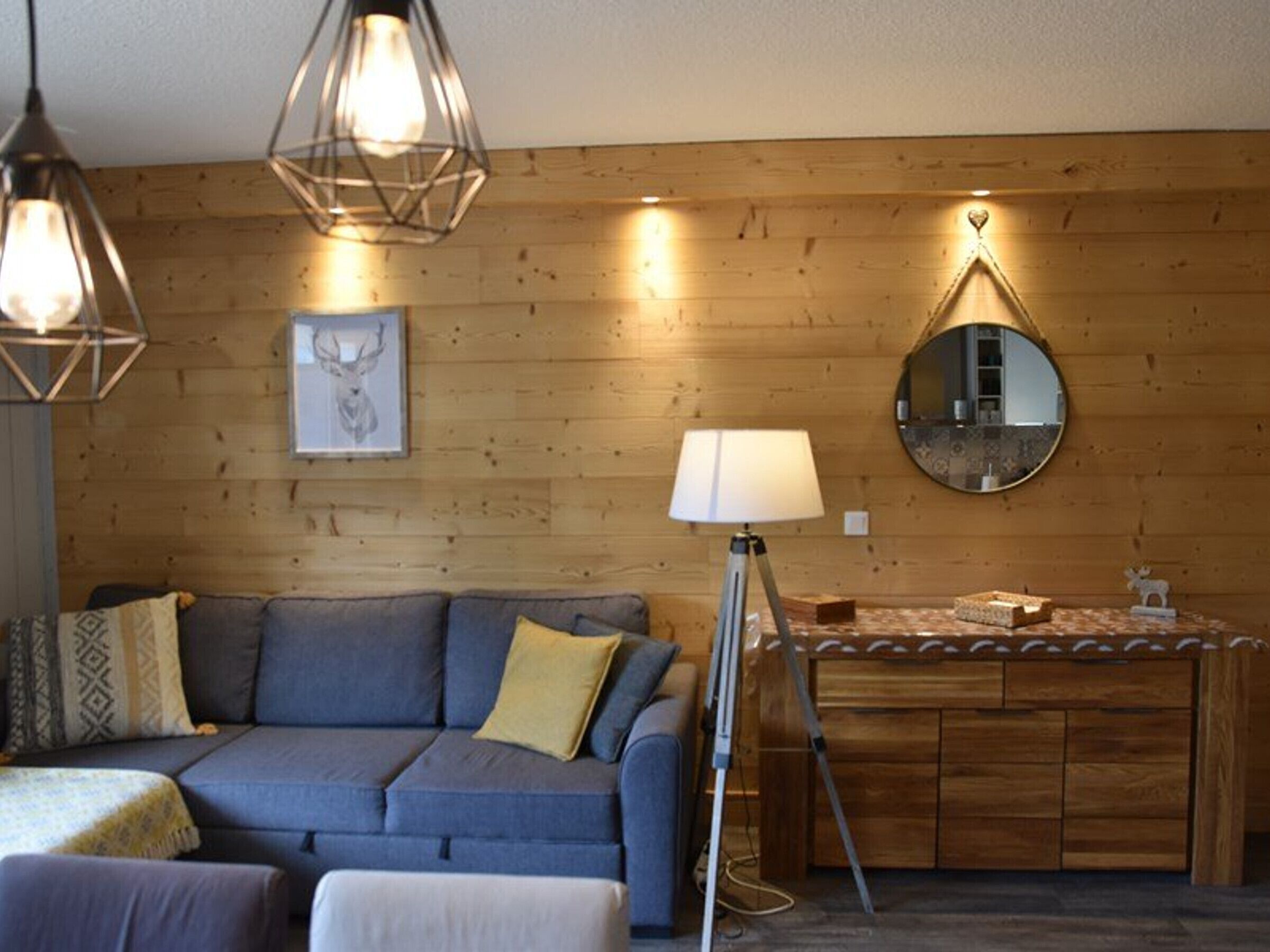Un salon chaleureux avec un mur en bois, un canapé bleu, une lampe sur pied et un miroir rond.