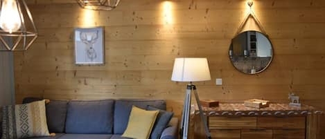 Ett mysigt vardagsrum med en väggpanel av trä, en blå soffa, en golvlampa och en rund spegel.