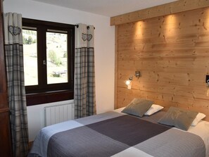 A bedroom with a wooden headboard, a bed with a grey and white checkered bedspread, two pillows, and a window with curtains. - Apartment with balcony and mountain view (Montgenèvre)