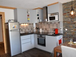 A compact kitchen with a refrigerator, microwave, oven, and a small dining area with a table and chairs. - Apartment with balcony and mountain view (Montgenèvre)