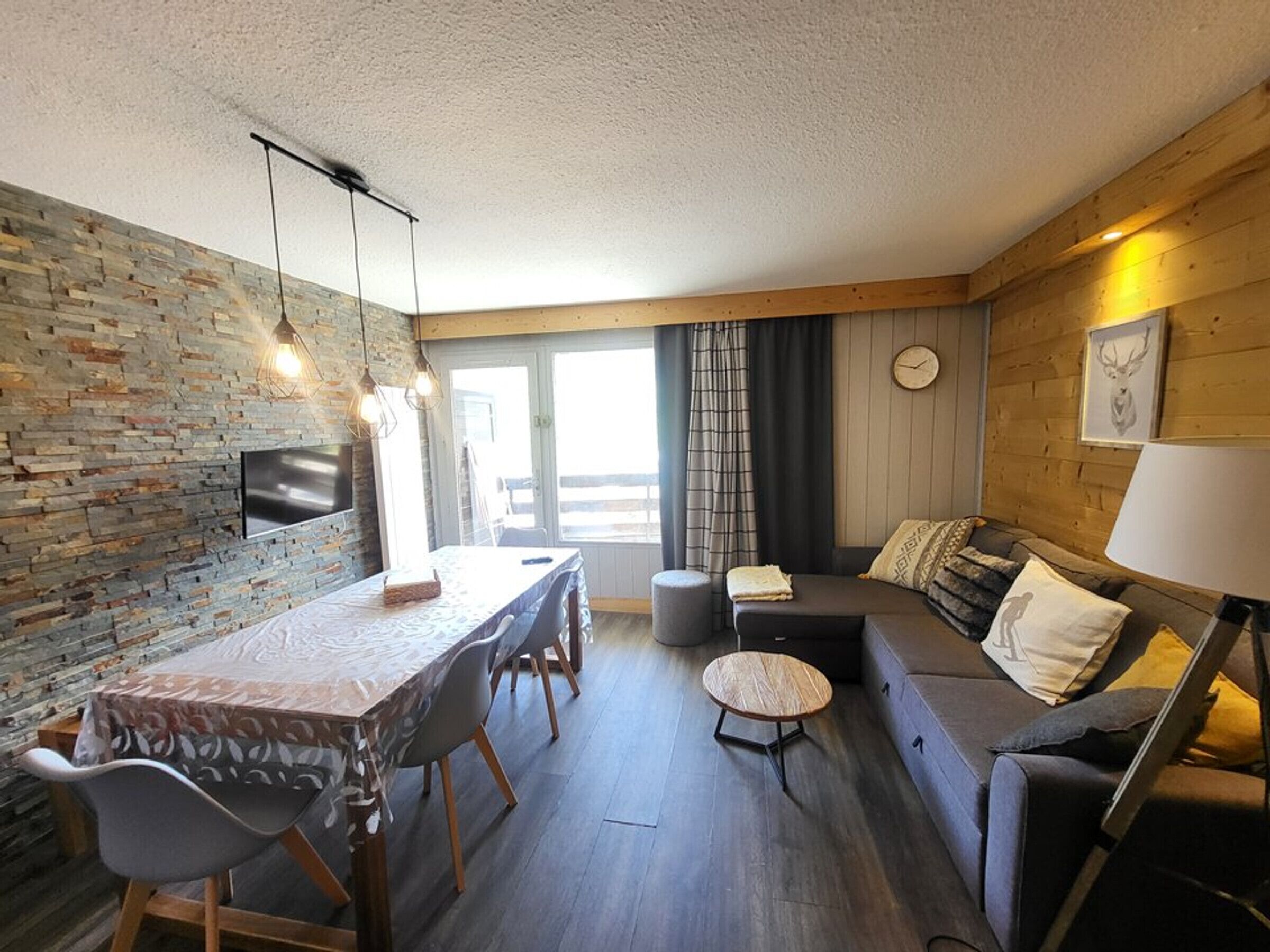 A modern interior with a dining area, sofa, and a television mounted on a stone wall.