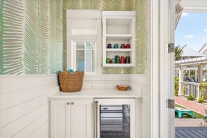 A kitchen with a window, a shelf with colorful containers, a basket, and a towel rack. - Poolside Pet-Friendly Cottage with Two King Suites & 20+ Amenities (Port Aransas)