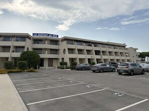 Un estacionamiento con varios autos, un edificio con un letrero que dice 'LE SERPENT DE MER', y un cielo despejado.