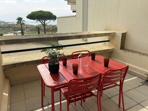 Ein roter Tisch und Stühle auf einem Balkon mit einem Blumentopf und einer klaren Glas-Kanne.