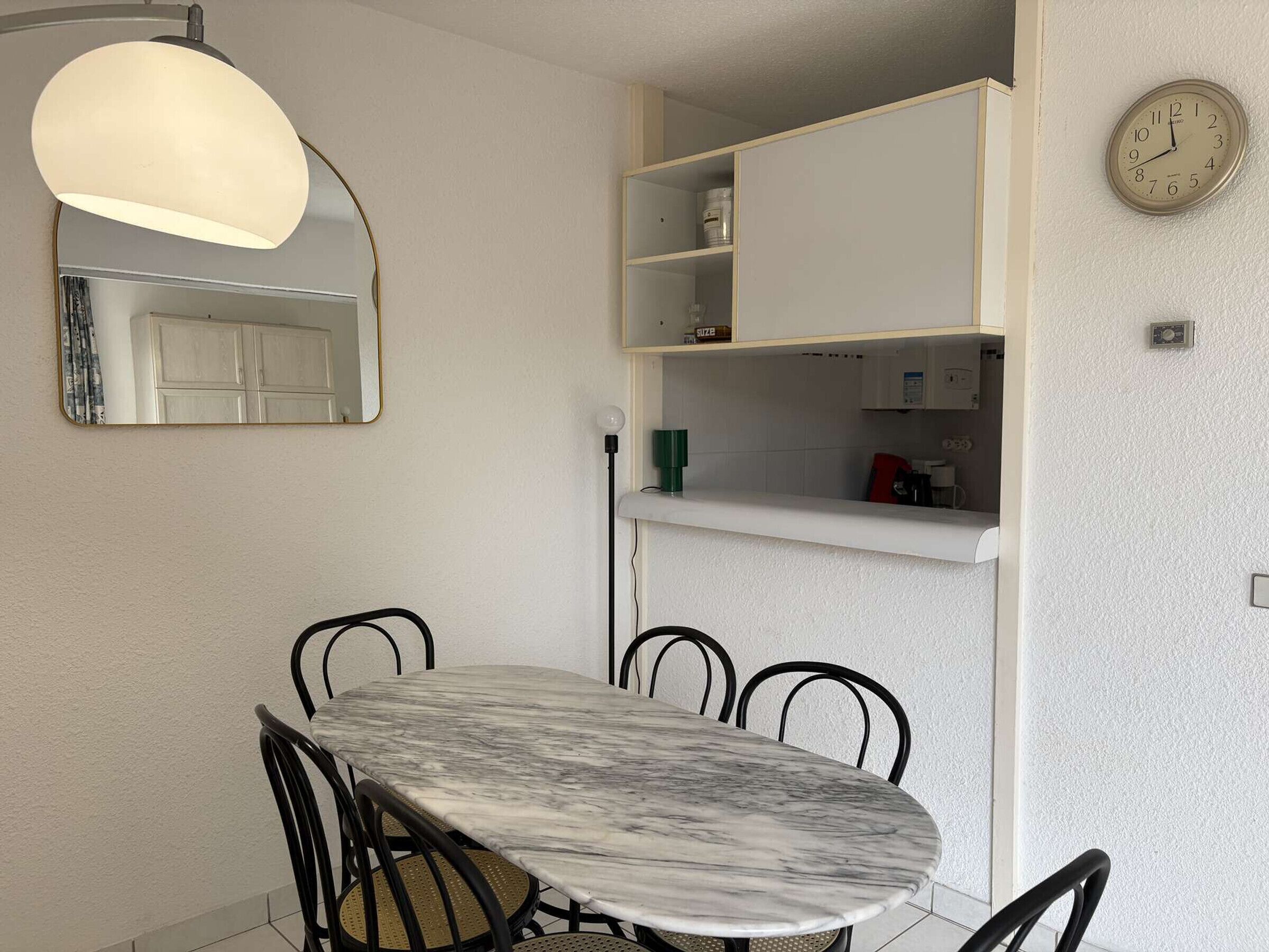 A dining area with a marble table, black chairs, a pendant light, a mirror, and a clock on the wall.