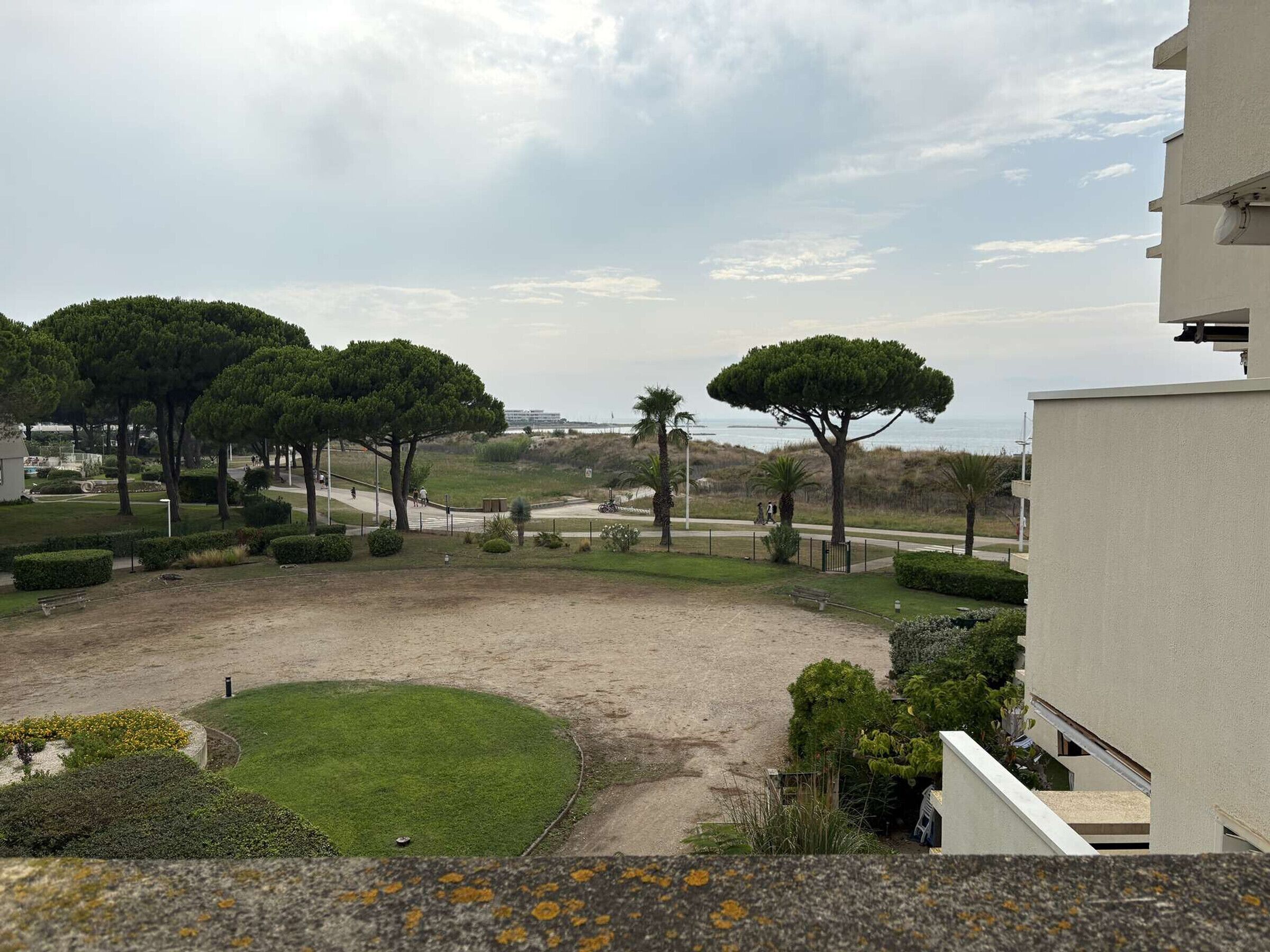 A residential area with a paved courtyard, trees, and a view of the sea.