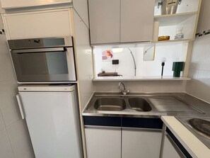 Eine kompakte Küche mit Einbauofen, Spüle und kleiner Arbeitsfläche.