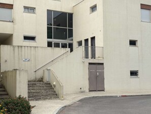 Ein Gebäude mit einer Betonfassade, einer Treppe, die zu einem Balkon führt, und einer Tür mit der Aufschrift 'LOCAL POUBELLER'.