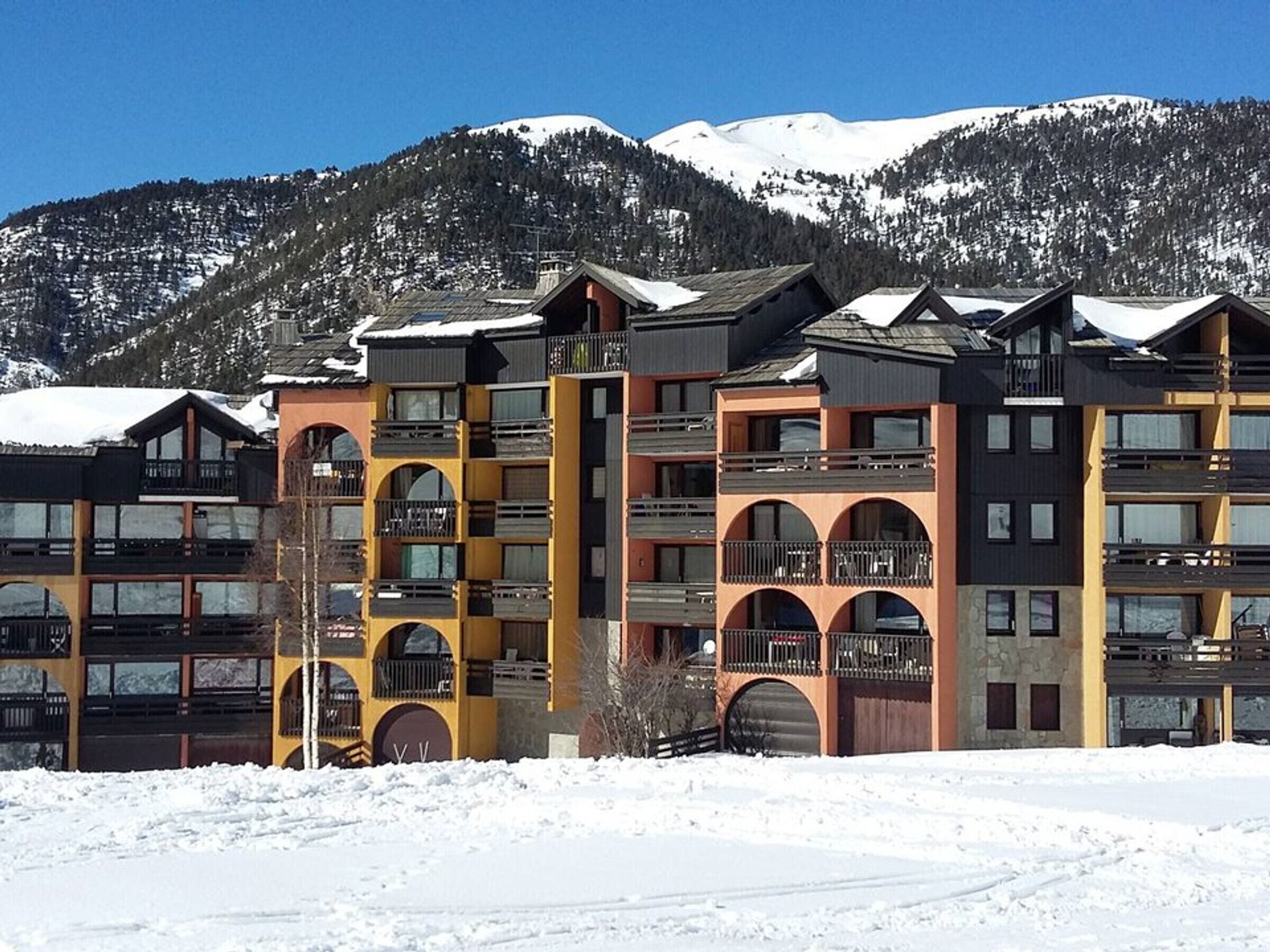 A multi-story hotel with balconies and a ski resort backdrop.