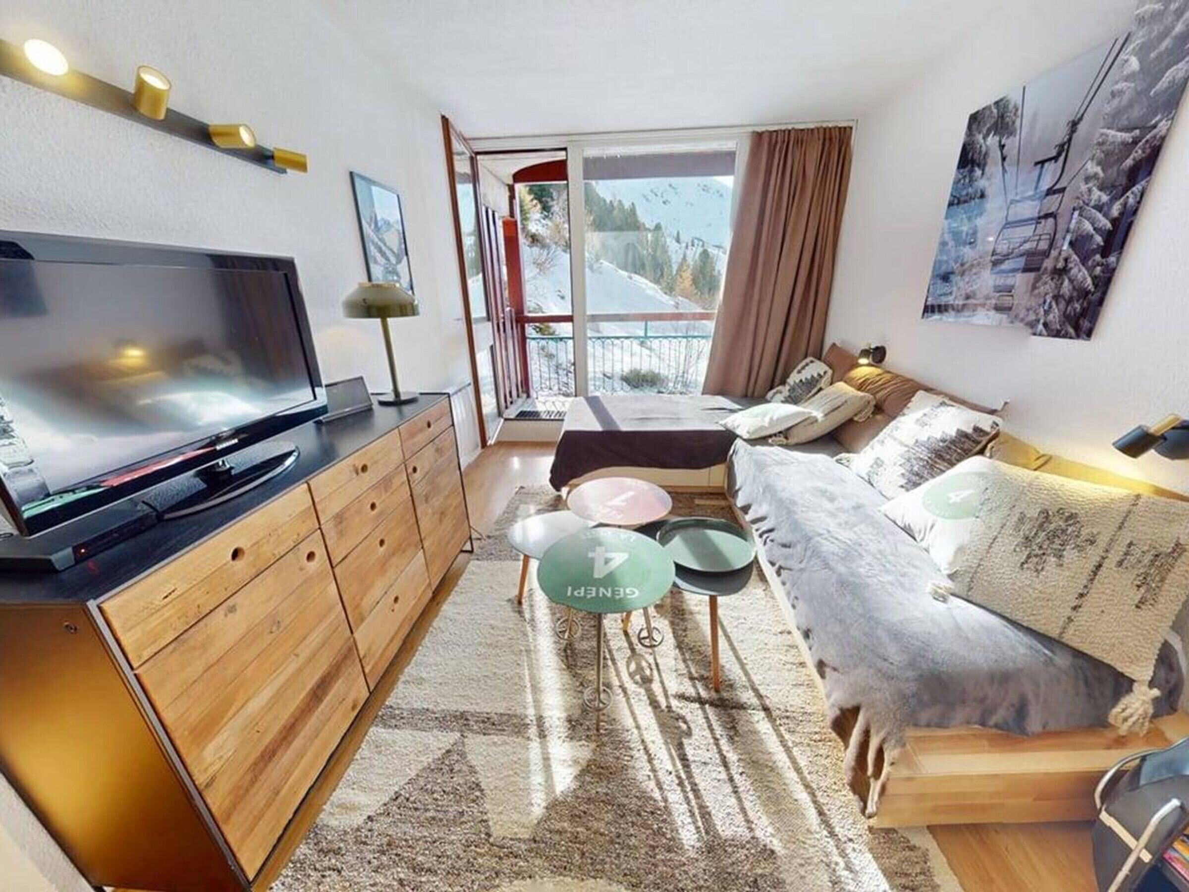 A modern living room with a flat-screen TV, wooden furniture, a sofa, and a balcony with a ski lift view.