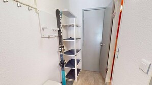 En smal gang med en hvid dør, en hvid væg med reolsystem og en hvid disk.