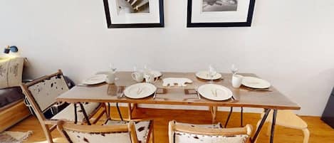 Uma sala de jantar com uma mesa de madeira posta para quatro pessoas, duas quadros na parede e cadeiras de estilo vintage.