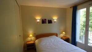 Hotellihuone, jossa on sänky, kaksi yöpöytälamppua, yöpöytä, ikkuna verhoilla ja seinään kiinnitetyt valaisimet.