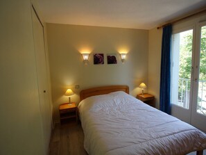 Ein Hotelzimmer mit einem Bett, zwei Nachttischlampen, einem Nachttisch, einem Fenster mit Vorhängen und Wandleuchten.