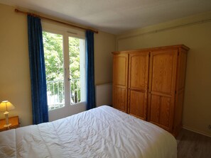 Ein Schlafzimmer mit Bett, Kleiderschrank, einem Fenster mit Vorhängen und einer Heizung.