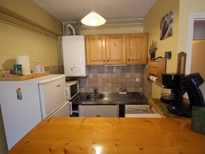 A compact kitchen with wooden cabinets, a sink, a stove, and a coffee maker. - Bright apartment with mountain view - 4 guests (Bagnères-de-Luchon)