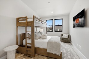 A bunk bed with a wooden ladder, a bedside table, and a chair in a room with two windows and a wall-mounted artwork. - Luxury 4BR | Free Ski Shuttle | Hot Tub | Deer Valley (Heber City)