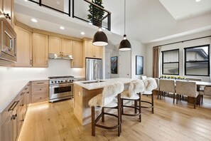 A modern kitchen with wooden cabinets, stainless steel appliances, and a central island with bar stools. - Luxury 4BR | Free Ski Shuttle | Hot Tub | Deer Valley (Heber City)