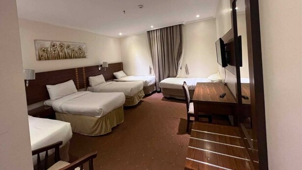 A hotel room with two beds, a desk, a TV, and a painting on the wall. - Reef Global Hotel Al Maabda (Makkah)