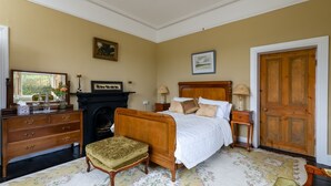 Ein traditionell eingerichtetes Schlafzimmer mit einem hölzernen Bett, einem Kamin, einem Schminktisch und einer Tür.