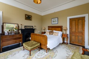 A traditional bedroom with a wooden bed, a fireplace, a dresser, and a door.