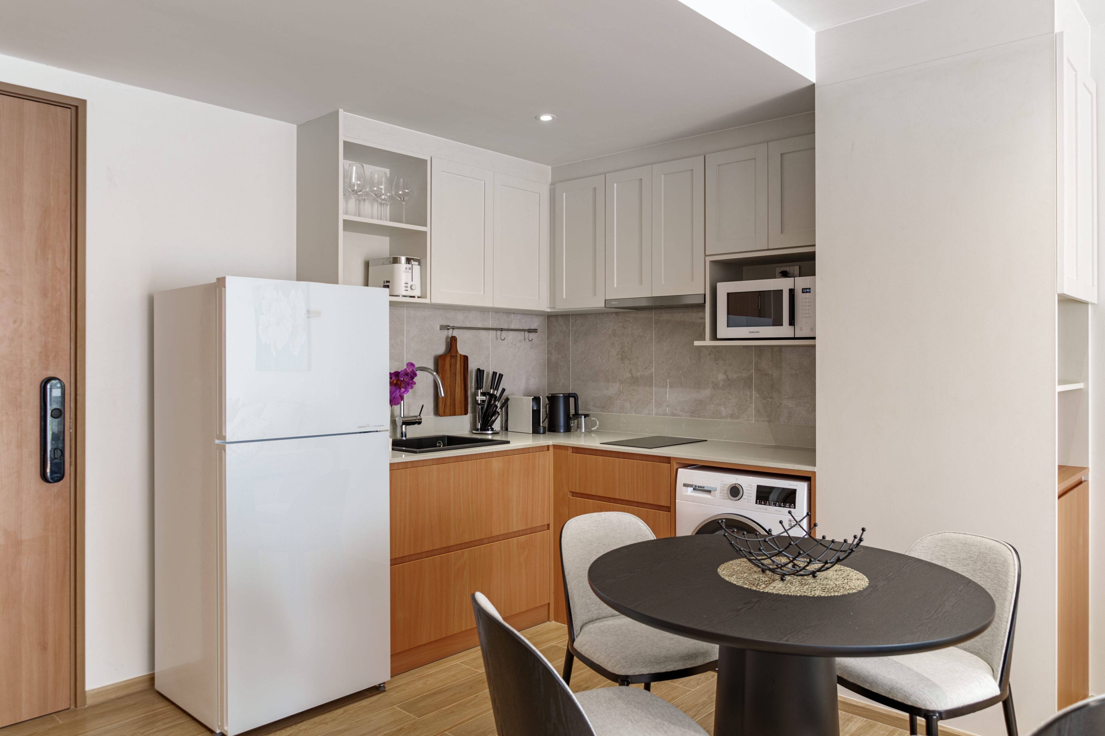 A compact kitchen with white cabinets, a built-in microwave, and a dining area with a round table and two chairs.