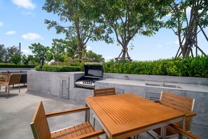 An outdoor patio with a built-in grill, seating area, and a view of trees and sky. - Laguna Beachside, 1BR • 200m to Bang Tao Beach (Choeng Thale)