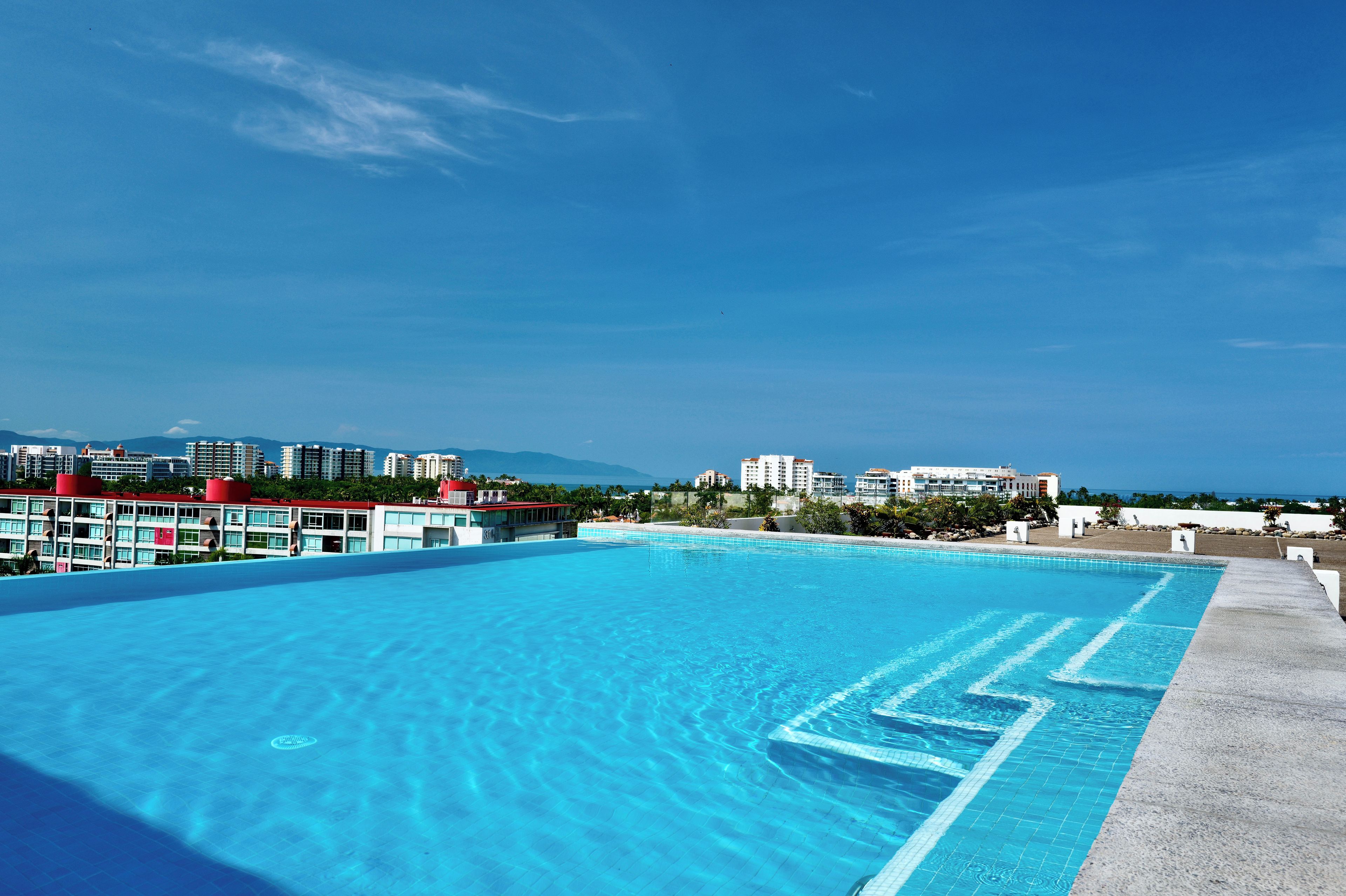 Una piscina cristallina blu con vista su uno skyline urbano e montagne sullo sfondo.