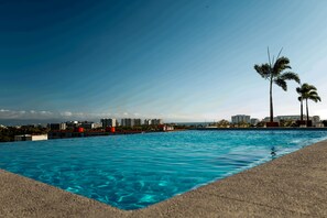 A swimming pool with clear blue water, surrounded by a concrete edge, and palm trees in the background. - Ideal Family Apartment with a Terrace and Pool in Nuevo Vallarta (Nuevo Nayarit)