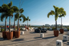 A rooftop terrace with potted palm trees, outdoor furniture, and a view of the cityscape. - Ideal Family Apartment with a Terrace and Pool in Nuevo Vallarta (Nuevo Nayarit)