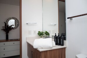 A bathroom with a large mirror, a sink with a towel, and toiletries. - Ideal Family Apartment with a Terrace and Pool in Nuevo Vallarta (Nuevo Nayarit)