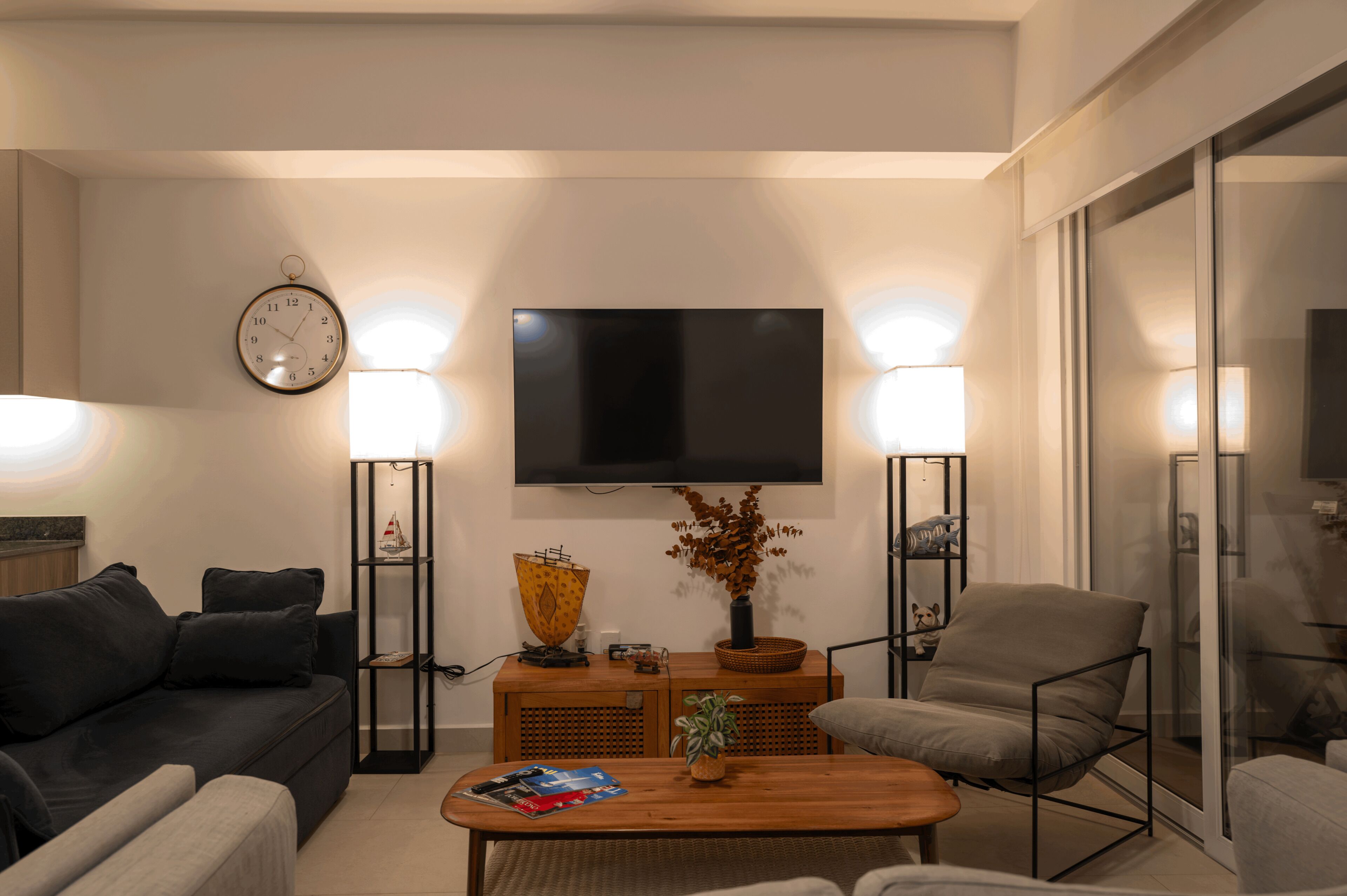 A modern living room with a sofa, armchair, coffee table, and a flat-screen TV mounted on the wall.