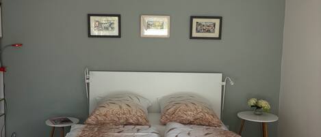Une chambre à coucher avec un lit double, une table de chevet avec une lampe, et trois tableaux encadrés accrochés au mur.