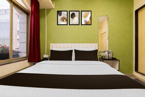 A hotel room with a large bed, a nightstand with a mirror, and three framed artworks on the wall. - Classic Malwade Motels (Pune)