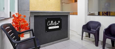 A reception area with a sign indicating it is a company-serviced collection point, two black chairs, and a decorative plant with red leaves.