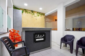 A reception area with a sign indicating it is a company-serviced collection point, two black chairs, and a decorative plant with red leaves. - Classic Malwade Motels (Pune)