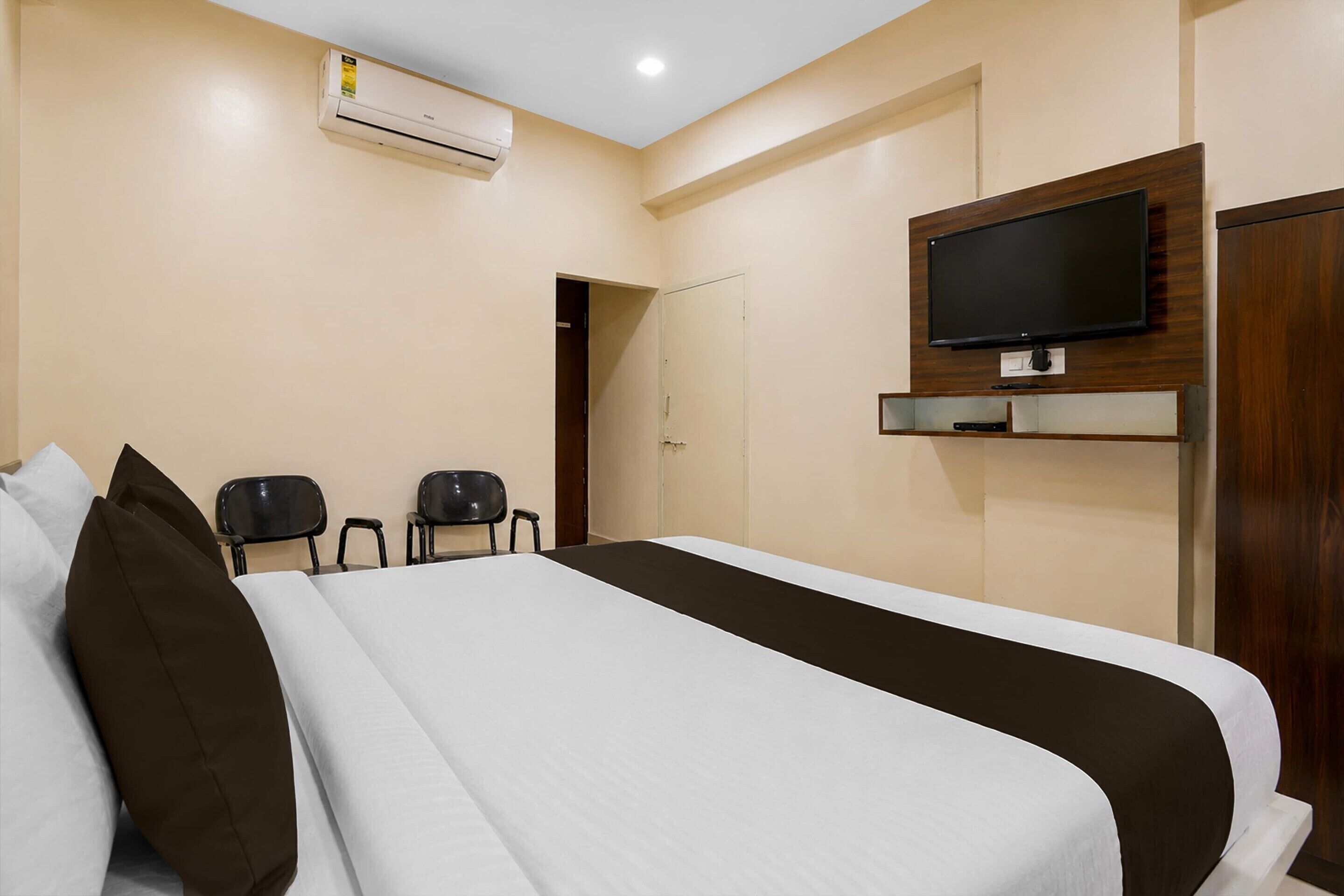 Una habitación de hotel con una cama, un televisor montado en la pared y una puerta que da a otra habitación.