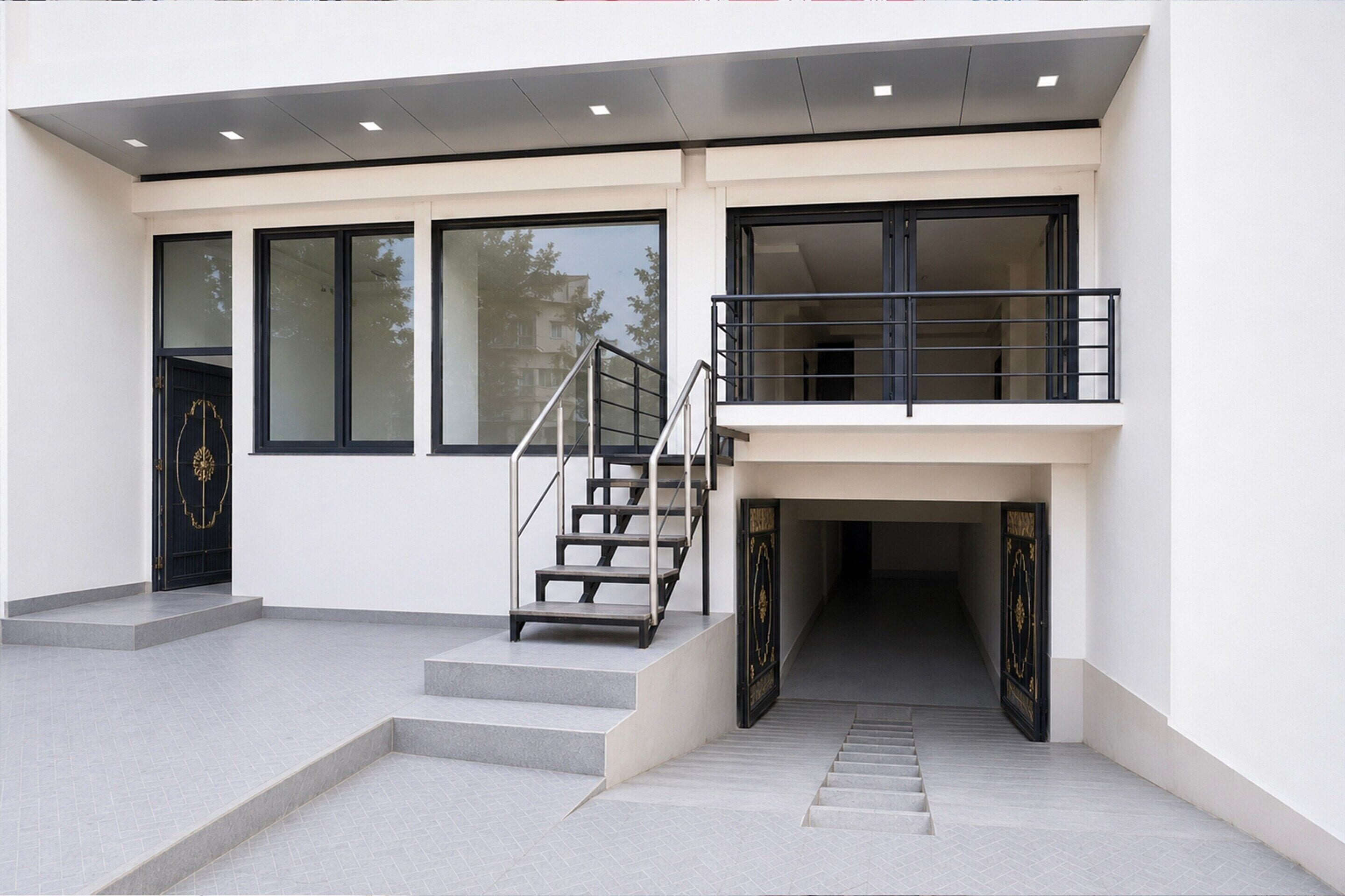 A modern building with a staircase leading to a balcony, large windows, and a black door.
