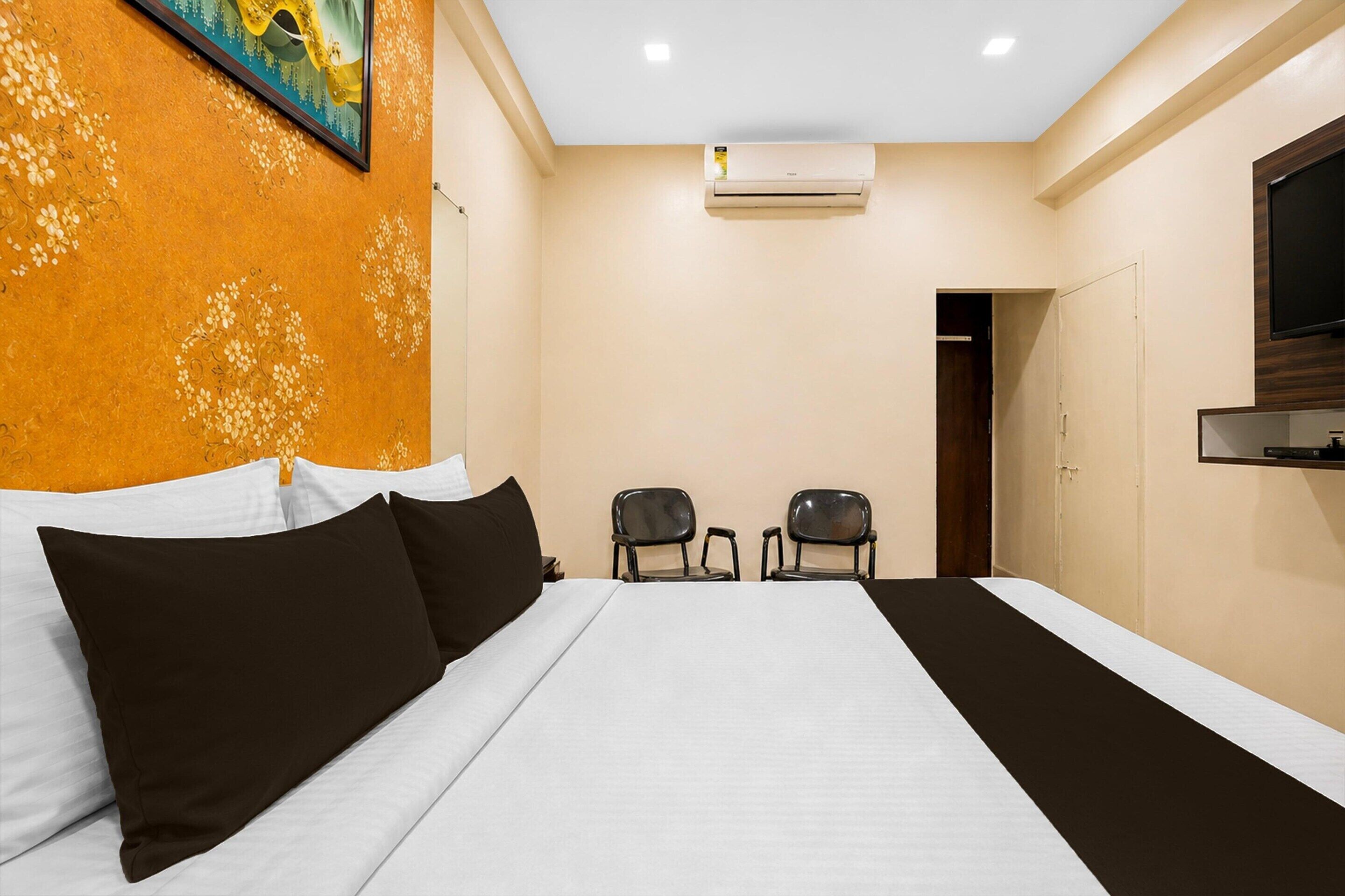 Une chambre d’hôtel équipée d’un lit, de deux chaises, d’un climatiseur et d’un téléviseur fixé au mur.