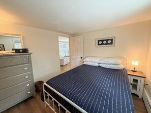 A bedroom with a bed, a dresser, a bedside table with a lamp, and a door leading to a balcony. - Nautical three bedroom sleeping 6 in West Dennis! (West Dennis)