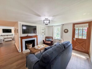A living room with a fireplace, a television, a sofa, and a wooden floor. - Nautical three bedroom sleeping 6 in West Dennis! (West Dennis)