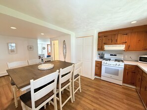 A kitchen with wooden cabinets, a white stove, and a dining table with chairs. - Nautical three bedroom sleeping 6 in West Dennis! (West Dennis)