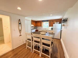 A compact kitchen with wooden cabinets, a central island, and a dining area with white chairs. - Nautical three bedroom sleeping 6 in West Dennis! (West Dennis)