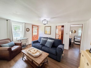 A living room with a sofa, coffee table, and a dining area with a chair and table. - Nautical three bedroom sleeping 6 in West Dennis! (West Dennis)