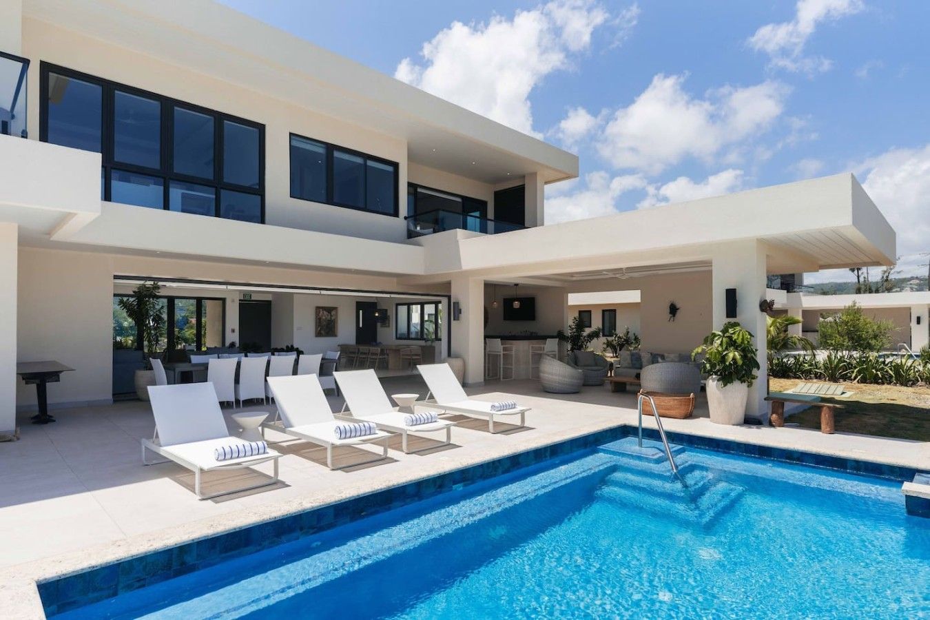 A modern two-story building with a swimming pool, outdoor seating, and a bar area.