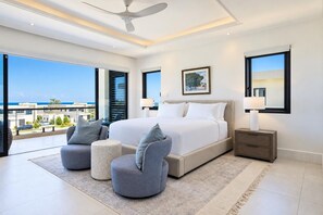 A modern bedroom with a large bed, two armchairs, a nightstand, and a ceiling fan. - Ocean View | 5BR Staffed Resort Villa by Bocobay (St. Ann’s Bay)